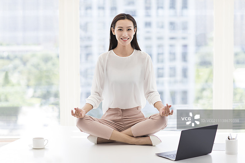 年轻商务女士坐在办公桌上练习瑜伽图片素材