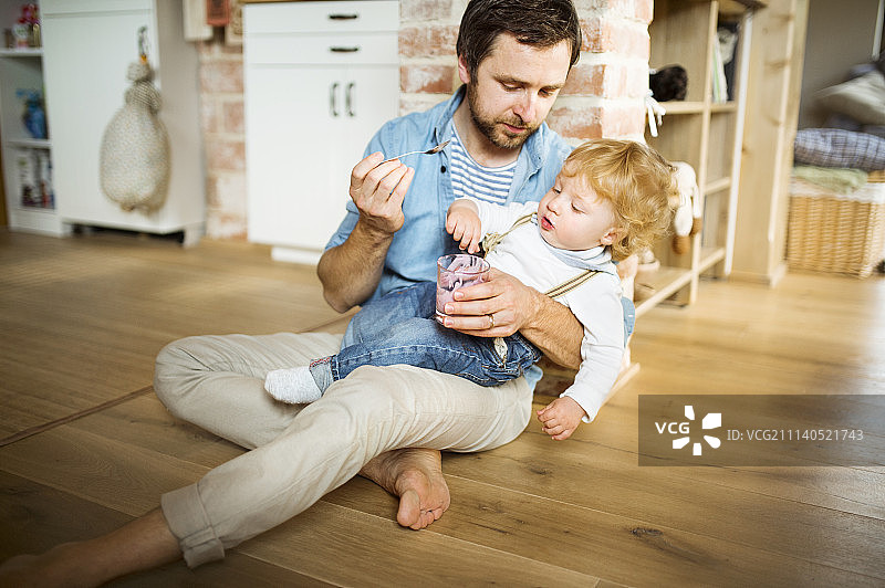 年轻的父亲在家喂他的小儿子吃酸奶图片素材