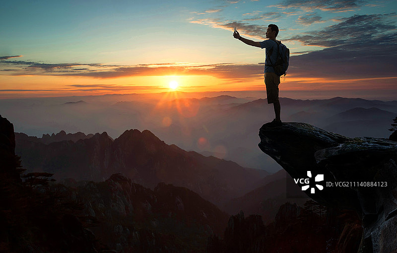 中年男人站在悬崖上拍照图片素材