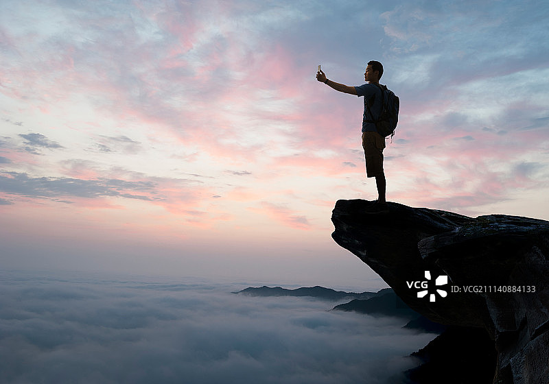 中年男人站在悬崖上拍照图片素材
