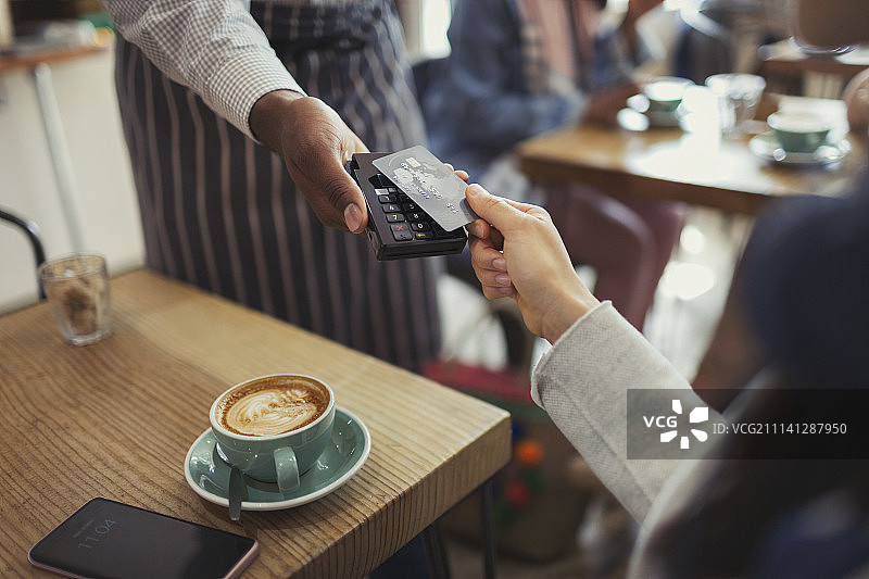 顾客在咖啡馆用信用卡非接触式支付给店员图片素材