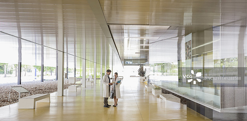 穿实验服的科学家在现代办公室大厅走廊交谈图片素材