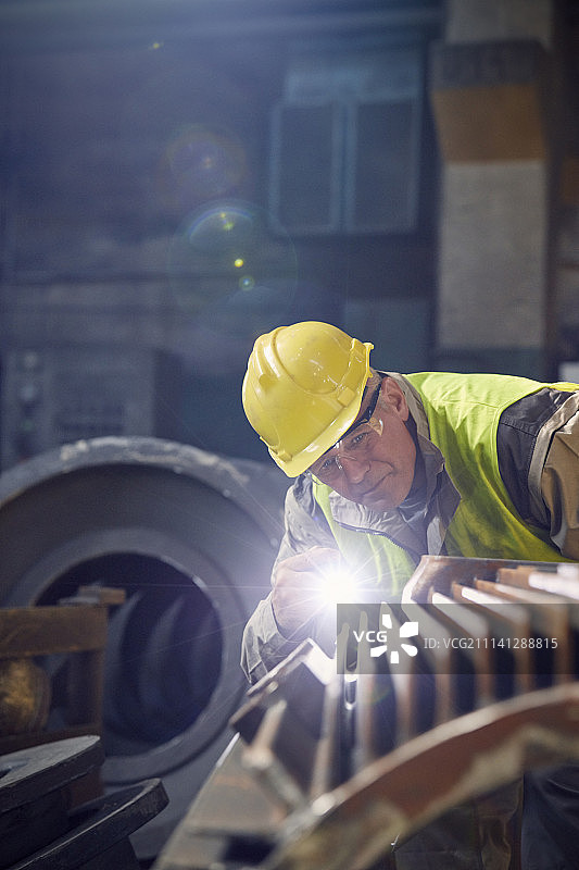 钢铁工人用手电筒检查钢铁厂的钢铁零件图片素材