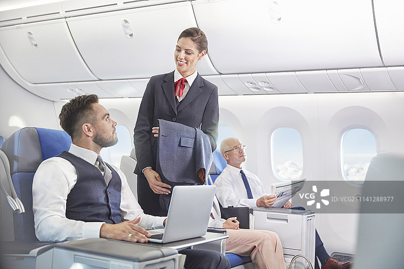 空乘人员与在飞机上用笔记本电脑工作的商人交谈图片素材