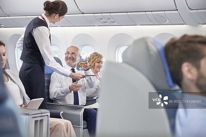 空乘在飞机头等舱为商人提供威士忌图片素材