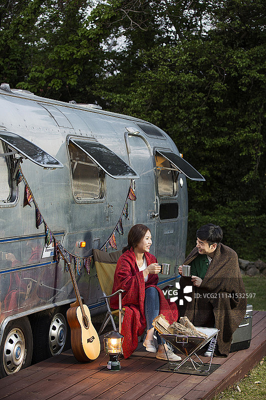 露营概念：年轻亚洲夫妇裹着毯子喝饮料图片素材