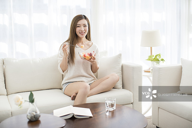 年轻女子在沙发上吃水果沙拉图片素材