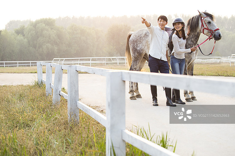 快乐的年轻情侣牵着马看向远方图片素材