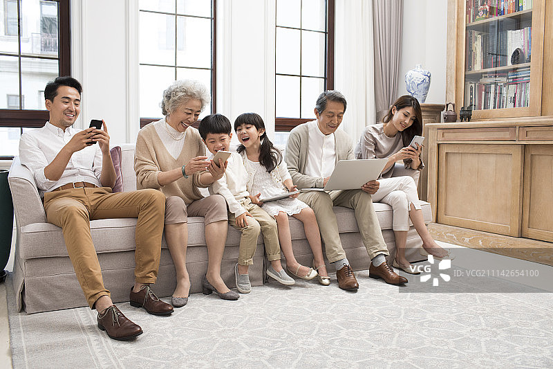 快乐家庭坐在沙发上玩电子产品图片素材