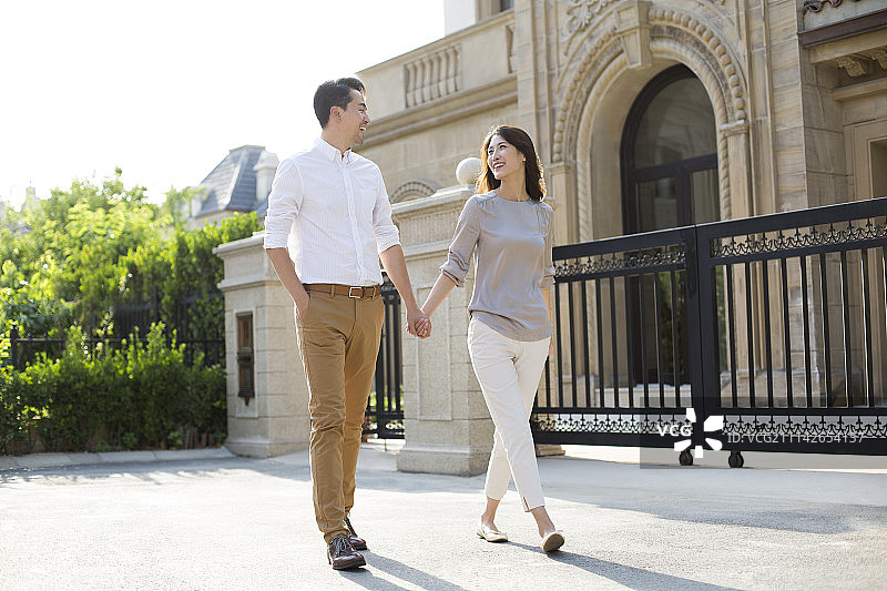 快乐的年轻夫妇手牵手在别墅外散步图片素材