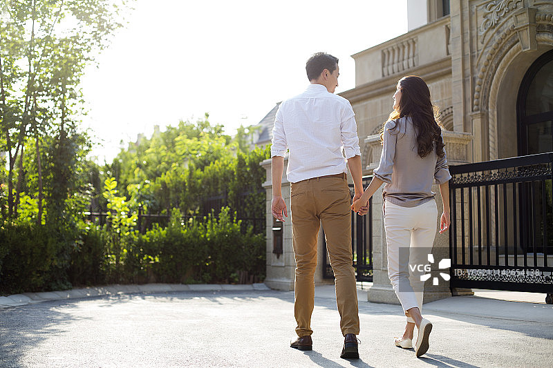 快乐的年轻夫妇手牵手在别墅外散步图片素材