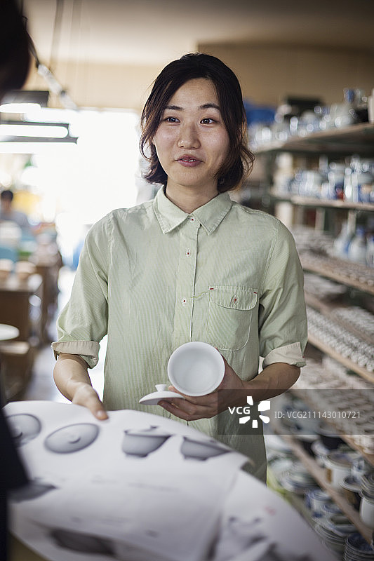 站在日本瓷器店里，拿着图纸和带盖杯子的微笑女人图片素材