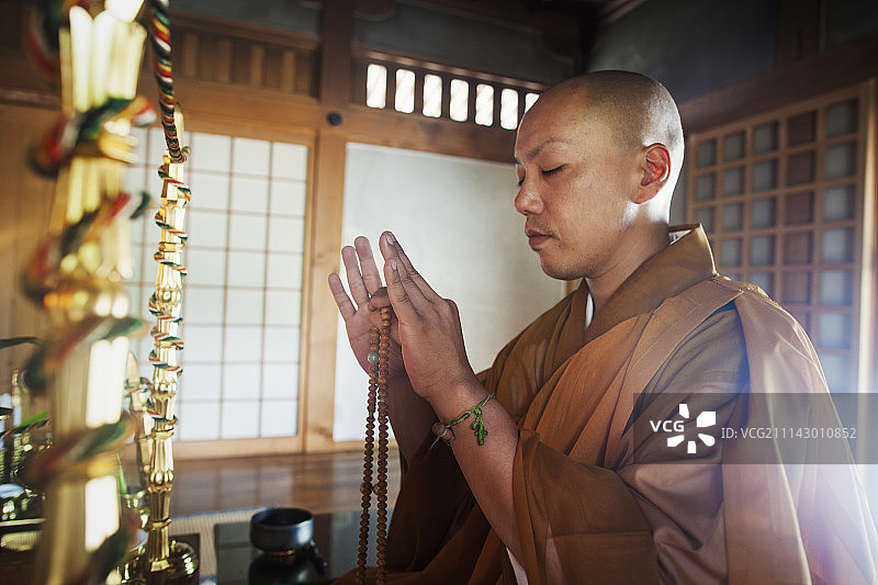 寺庙内，侧面视角下的僧侣跪地手持佛珠，闭目冥想图片素材