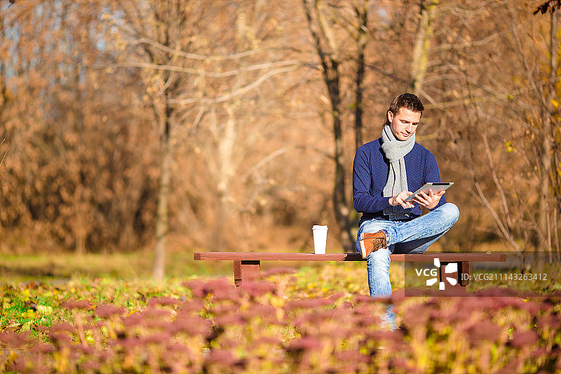 年轻男人秋日公园户外喝咖啡玩手机图片素材