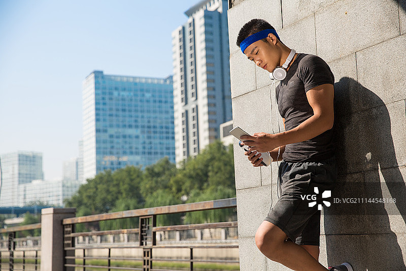 年轻男子运动后休息玩手机图片素材