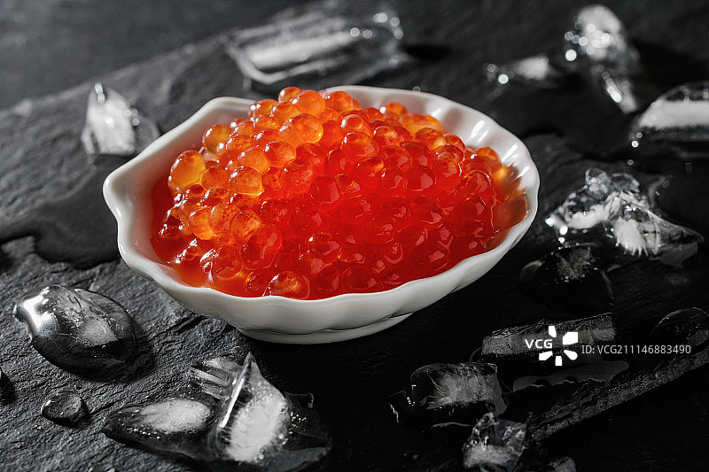 黑色湿页岩板上贝壳形白色碗中的红色鱼子酱图片素材