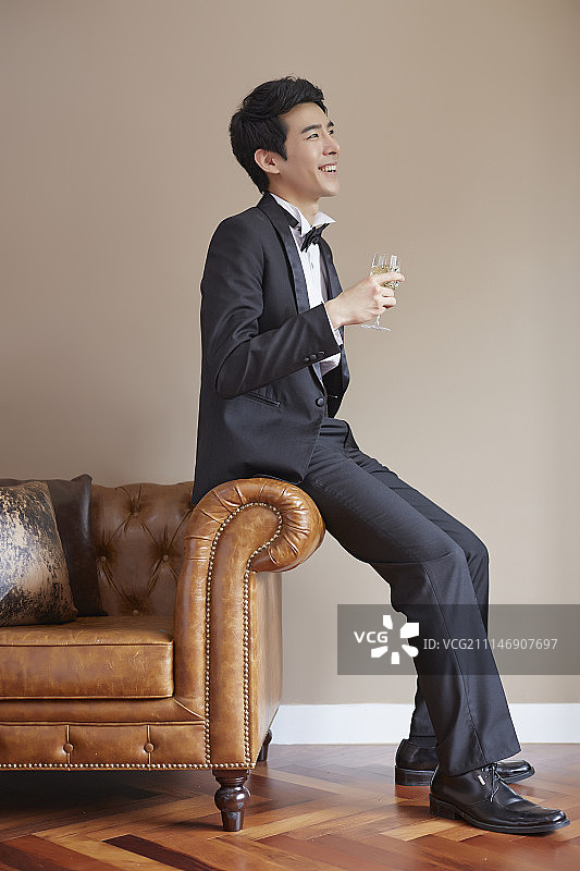 身穿燕尾服的男子坐在沙发上拿着香槟酒杯摄影图片素材