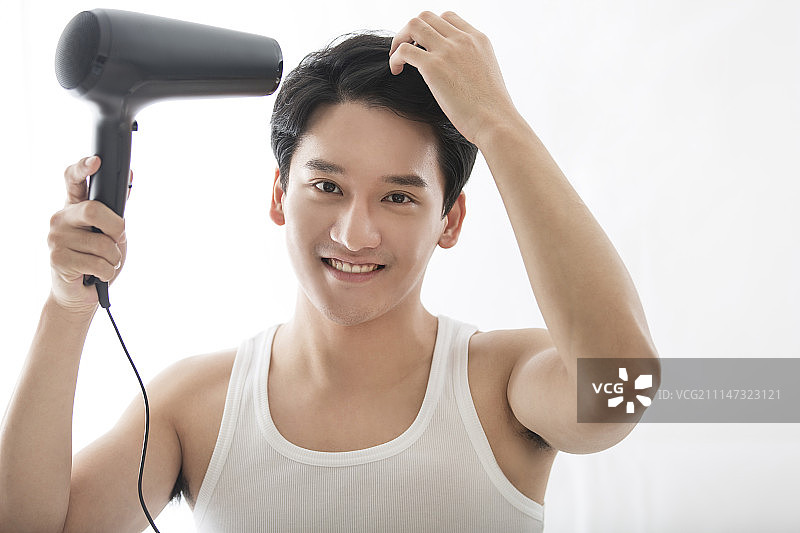 年轻男子用吹风机吹头发图片素材