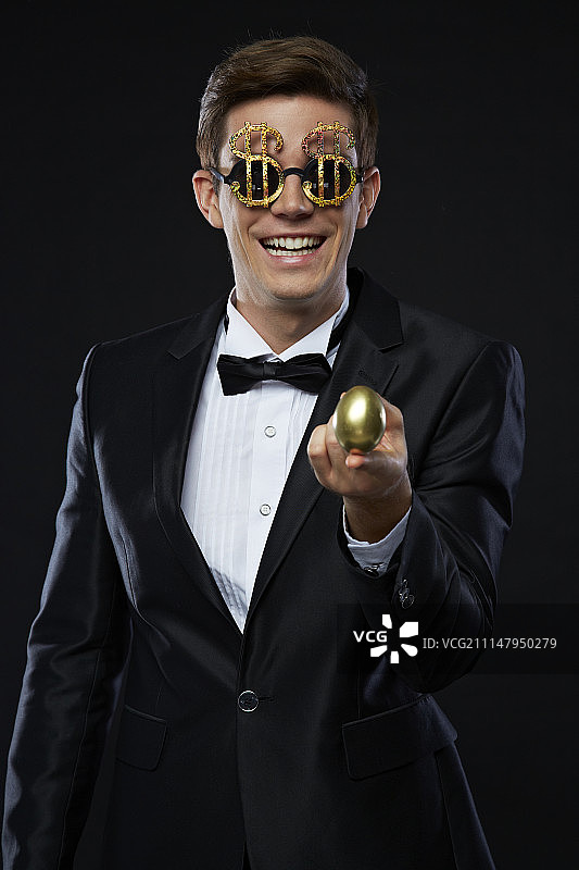 身穿燕尾服、戴着美元眼镜、 holding 金蛋的男子的摄影作品图片素材