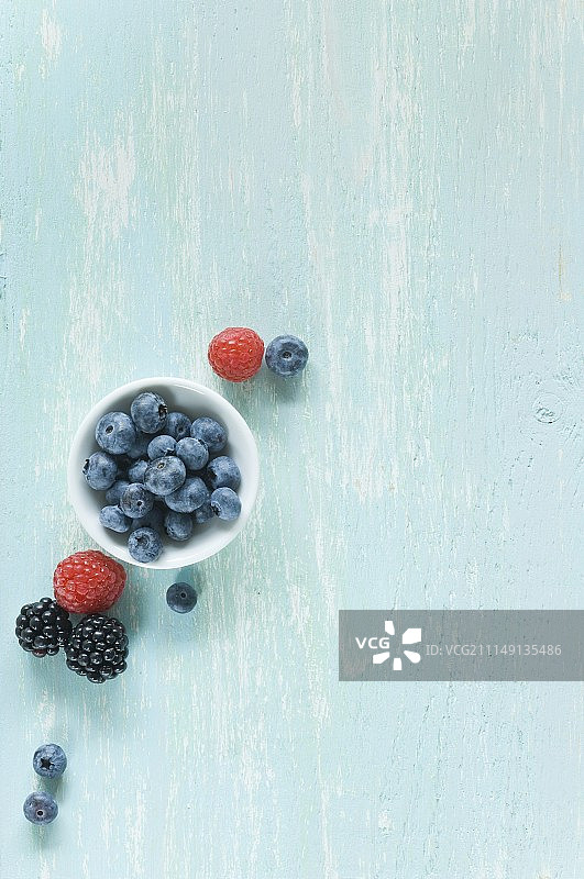 小碗蓝莓，旁边桌上有覆盆子和黑莓图片素材