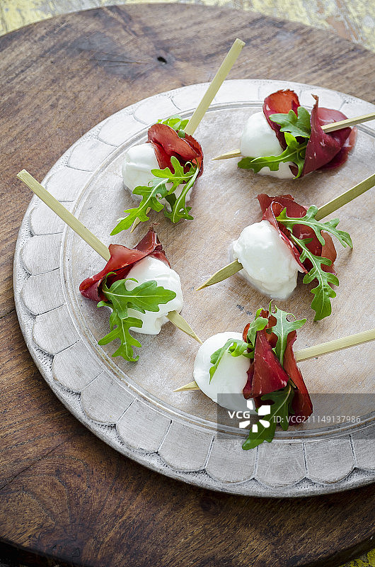 白木板上搭配布雷萨奥拉和新鲜芝麻菜的水牛马苏里拉奶酪小吃图片素材
