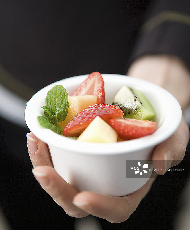 手拿盛有什锦水果沙拉的小白球图片素材