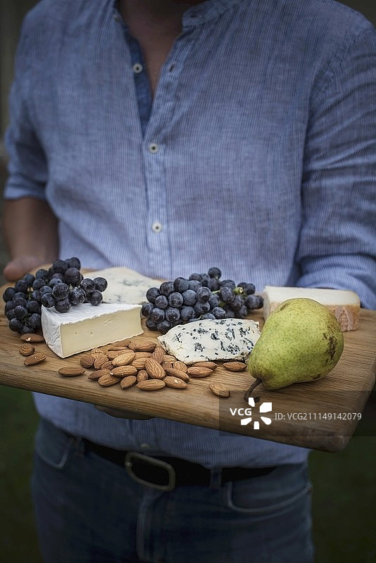 男人拿着装有葡萄、梨和杏仁的奶酪板图片素材