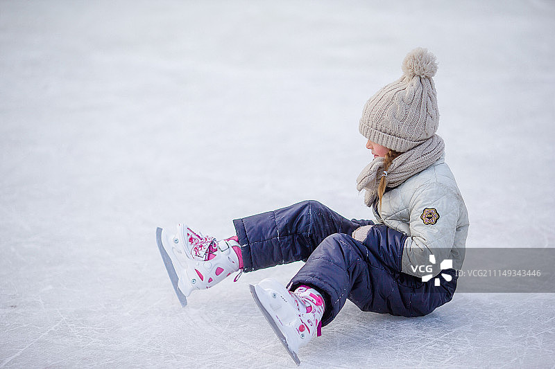 摔倒后坐在冰上，穿着溜冰鞋的可爱小女孩图片素材