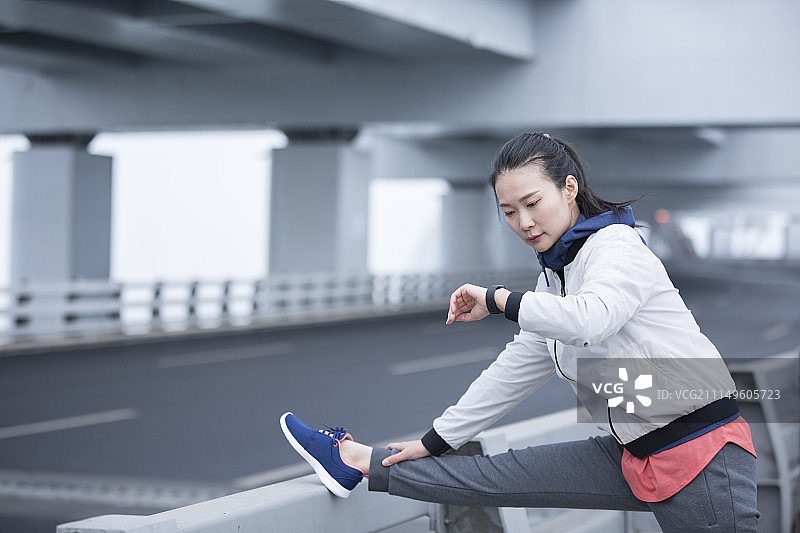 青年女子在户外查看智能手表做形体训练图片素材