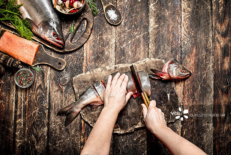 生鱼片：女性在旧木桌上切割新鲜的三文鱼图片素材
