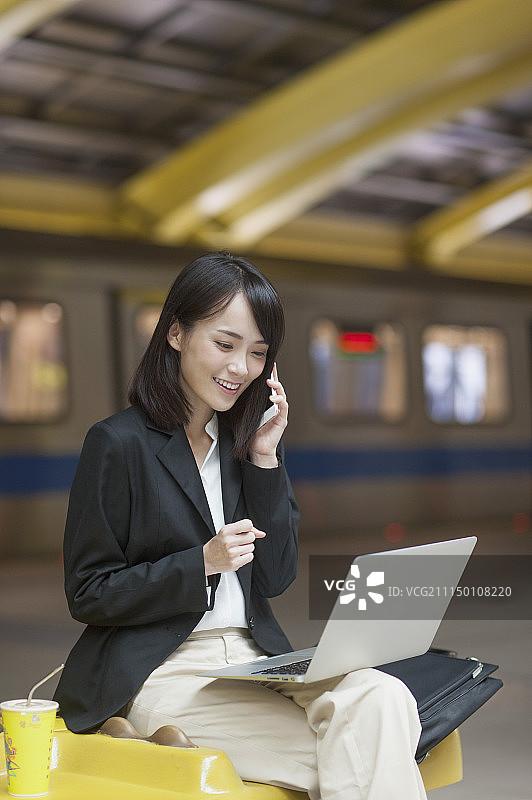 一位办公女性边打电话边使用笔记本电脑图片素材