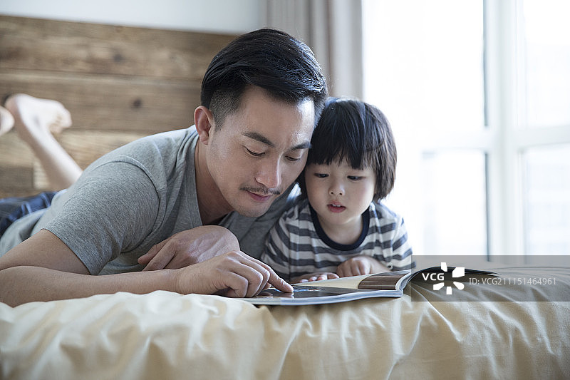 小男孩和爸爸在床上看书图片素材