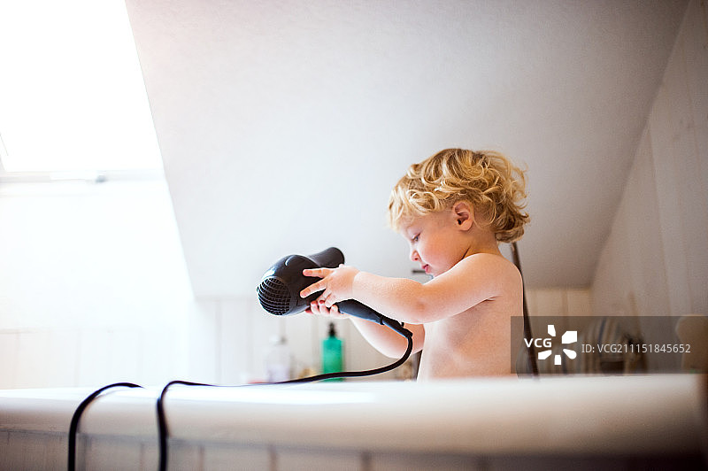 在浴室浴缸里拿着吹风机的幼儿男孩图片素材
