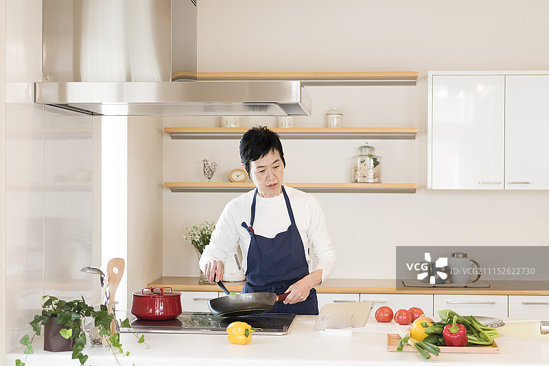 年长妇女用平板电脑做饭图片素材