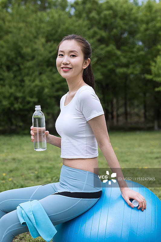 坐在健身球上喝水的年轻女性图片素材