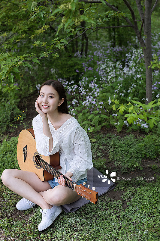 坐在草地上弹吉他的年轻女孩图片素材