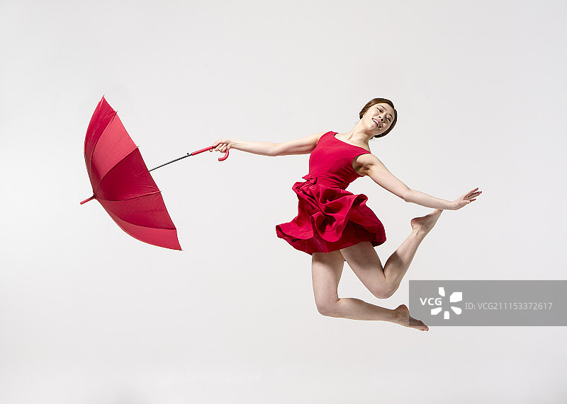 在白色背景上赤脚持伞跳舞的红裙女子摄影图片素材