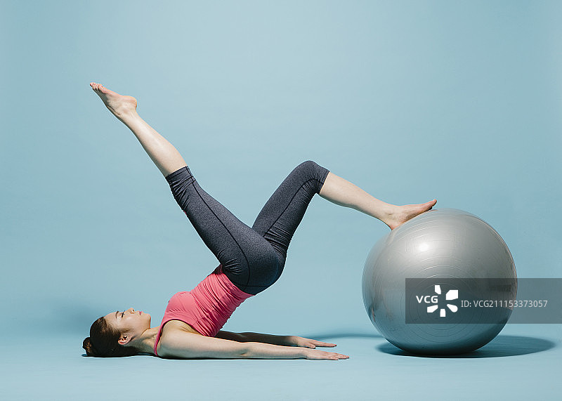 在蓝色背景上用球做拉伸运动的运动装女子摄影图片素材