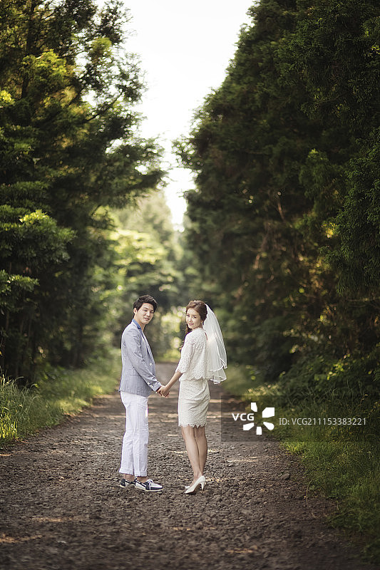 新娘和新郎在森林中手牵手同行并回头看图片素材