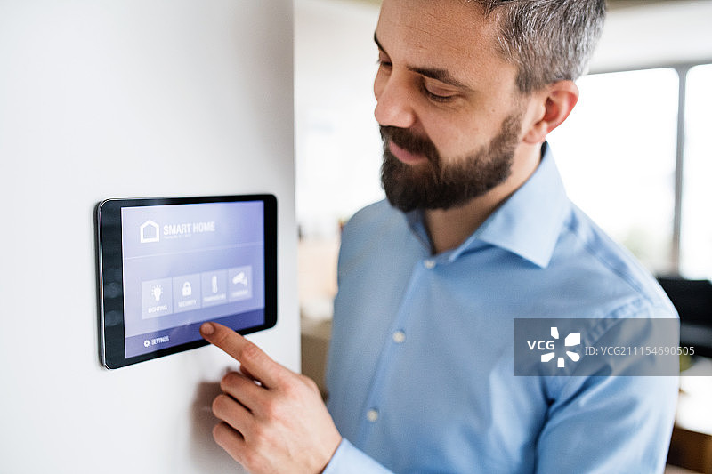 男子在家中指向带有智能家居屏幕的平板电脑图片素材
