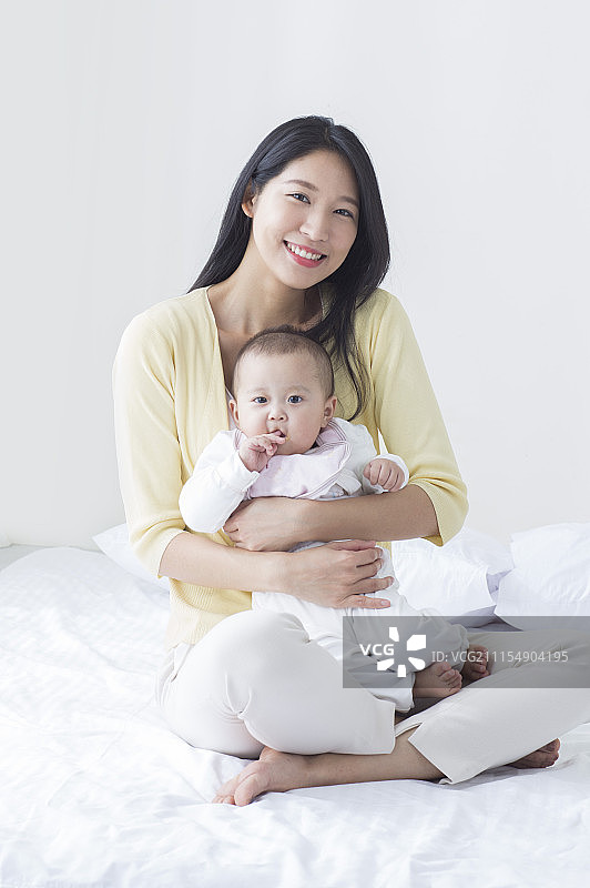 年轻妈妈坐在床上抱着宝宝图片素材