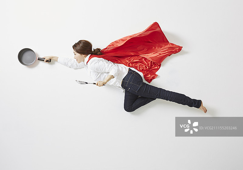 穿着红色斗篷像女超人一样拿着炊具飞翔的女人摄影图片素材