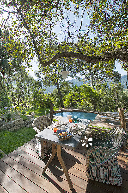 藤椅环绕着木制露台上摆放的早餐桌，背景是游泳池图片素材