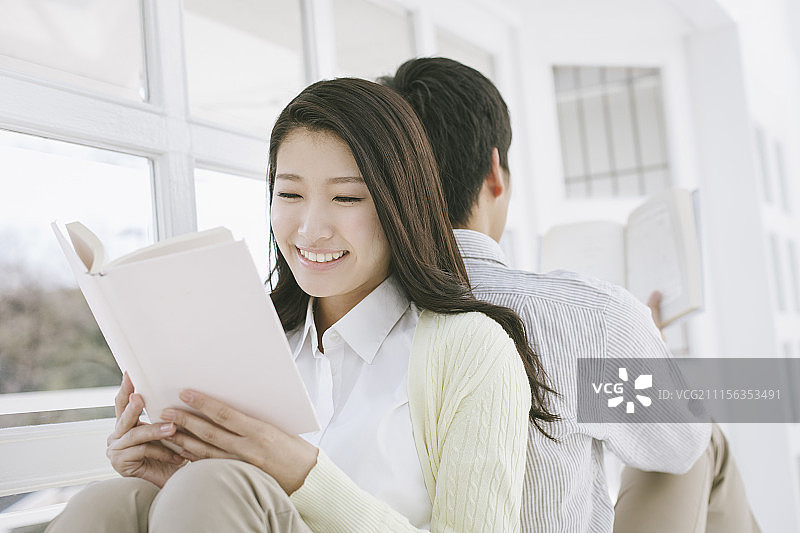 情侣背靠背坐在窗边读书摄影图片素材