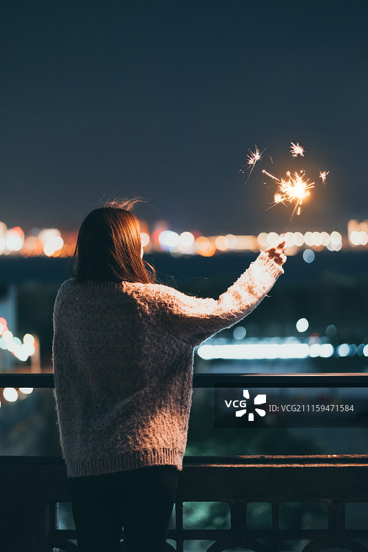 在夜幕霓虹下燃放烟火的少女图片素材
