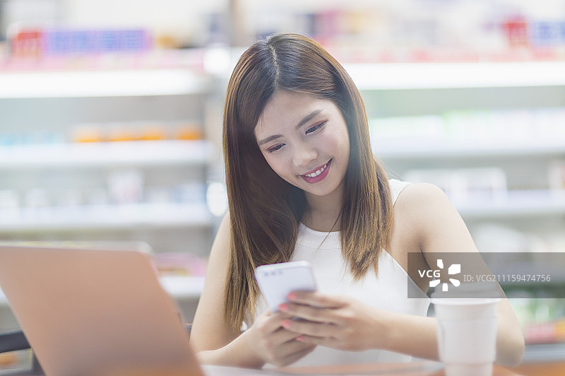 年轻女人坐在便利商店使用手机图片素材