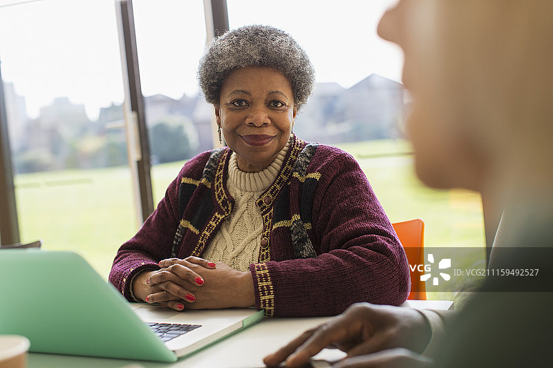 在会议室里使用笔记本电脑的自信微笑的年长女商人图片素材