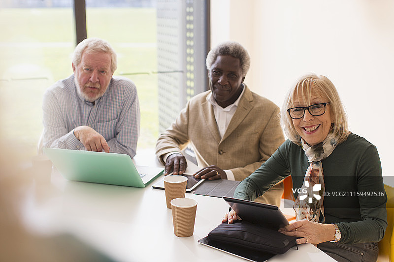 微笑的高级商务人士在会议室里使用平板电脑和笔记本电脑开会图片素材