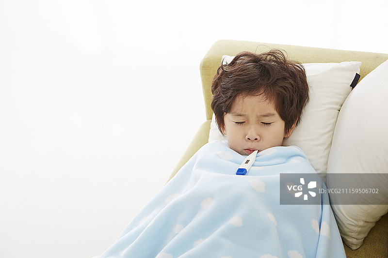 生病的小男孩躺在沙发上，盖着毯子摄影图片素材