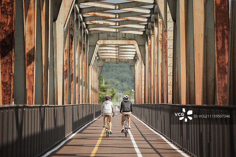 情侣戴着头盔骑自行车经过桥的摄影照片图片素材